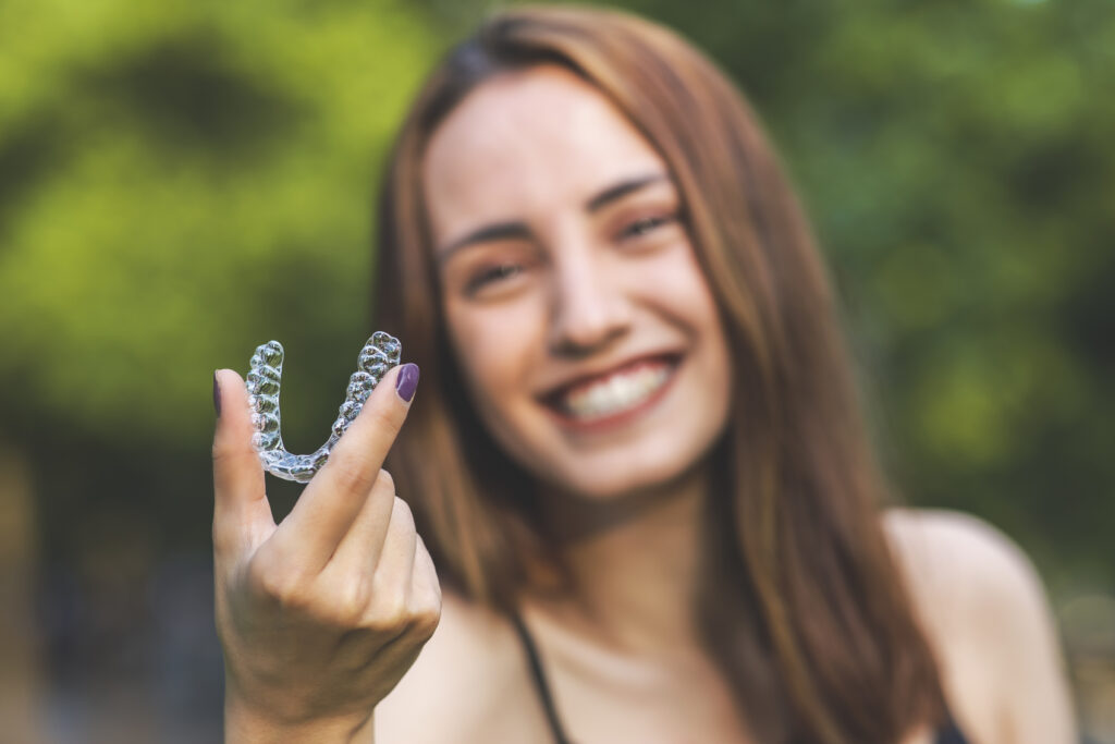 smiling woman holding up clear retainers to straighten teeth