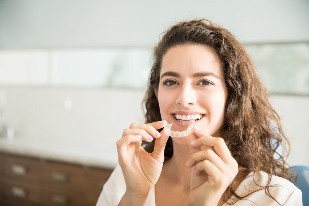 patient happily holding clear teeth aligners to help treat teeth alignment issues